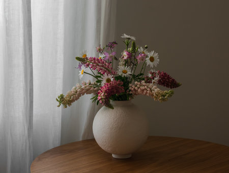 Summer bouquet of garden wildflowers, daisies, lupines in a ceramic vase on a wooden tableの写真素材