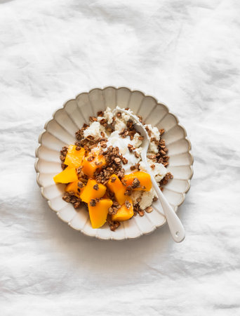 Cottage cheese with Greek yogurt, mango and crispy granola - delicious breakfast on a light background, top viewの写真素材