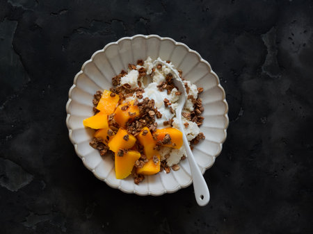 Cottage cheese with Greek yogurt, mango and crispy granola - delicious breakfast on a dark background, top viewの写真素材
