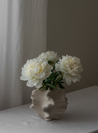 Bouquet of white peonies in a creative ceramic vase on the tableの写真素材