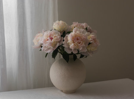 A bouquet of white peonies in a ceramic vase on a table with a white tablecloth in the living roomの写真素材