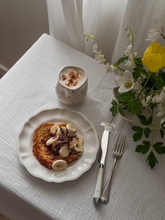 Cozy homemade breakfast - French toast with banana and chocolate, coffee, bouquet of flowers on the table in the living room by the windowの写真素材