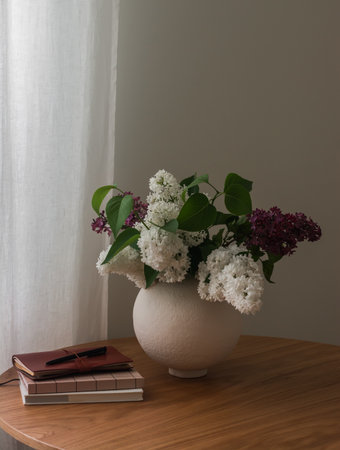 A bouquet of lilacs in a ceramic vase, notebooks. books on a wooden tableの写真素材