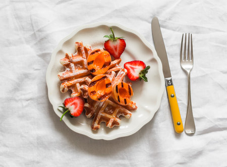 Traditional Belgian waffles with caramelized apricots and strawberries - a delicious dessert on a light background, top viewの写真素材