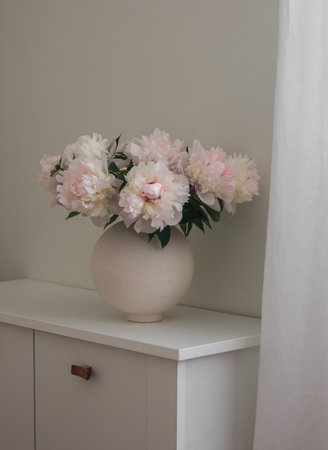 Bouquet of white peonies in a ceramic vase on a white chest of drawers in the living roomの写真素材