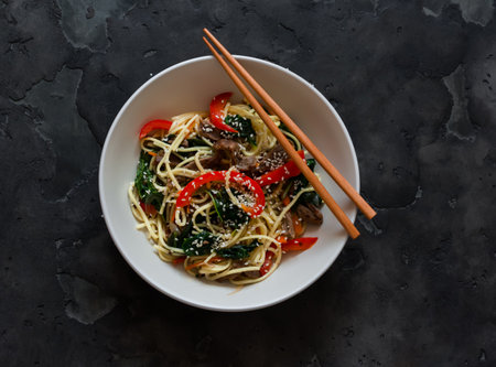 Noodles with beef, spinach and vegetables in Asian style on a dark background, top viewの写真素材