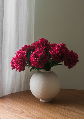 Bouquet of peonies in a round ceramic vase on a wooden table in the living roomの写真素材