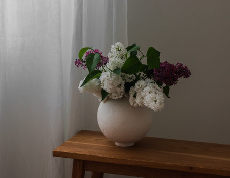 A bouquet of lilacs in a round ceramic vase on a wooden console in the living roomの写真素材