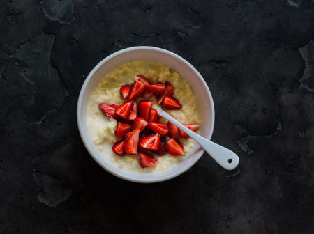 Millet porridge with fresh strawberries in a bowl on a dark background, top view