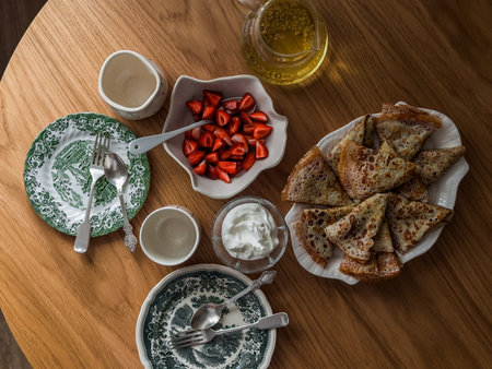 Delicious breakfast, brunch - crepes, cream, fresh strawberries, green tea on a round wooden tableの写真素材