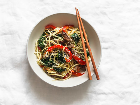 Noodles with beef, spinach and vegetables in Asian style on a dshpre background, top view