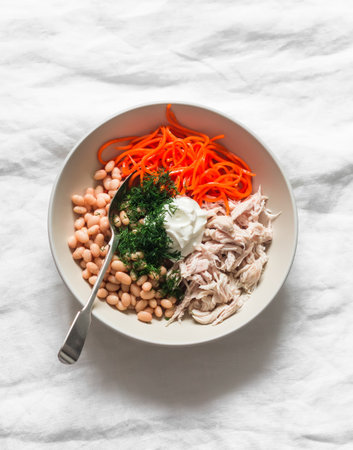 The idea of the salad - canned beans, boiled chicken fillet, spicy carrots, natural yogurt and dill in a bowl on a light background, top viewの写真素材