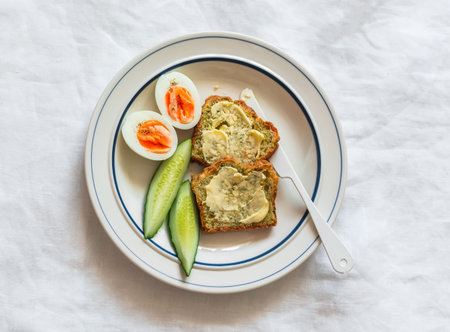 Delicious breakfast - toasts with butter, boiled egg, fresh cucumber on a plate on a light...
