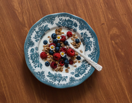 Greek yogurt with granola, raspberries and blueberries in a vintage plate on a wooden table
