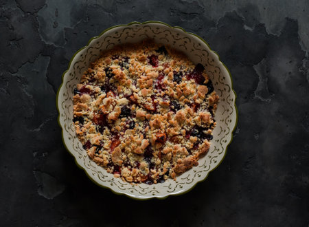 Apricots, cherries, strawberries crumble in a baking dish on a dark background, top view