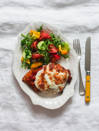Chicken with tomato sauce and mozzarella and fresh vegetable salad on a light background, top view