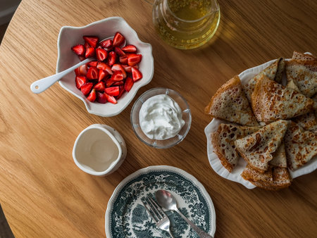 Breakfast served with crepes, fresh cream and strawberries on a wooden table, top viewの写真素材