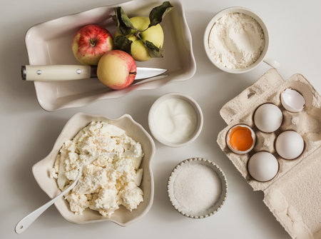 Ingredients for making a curd casserole for breakfast - cottage cheese, apples, sour cream, sugar on a light background, top viewの写真素材