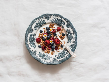 Greek yogurt with granola, raspberries and blueberries in a vintage plate on a white backgroundの写真素材