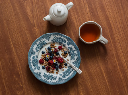 Natural greek yogurt with crispy granola, raspberries and blueberries and tea on a wooden table, top view. Delicious breakfastの写真素材