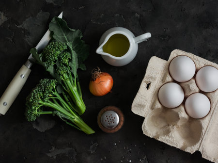Breakfast ingredients - eggs, broccoli, olive oil, pepper on a dark background, top view