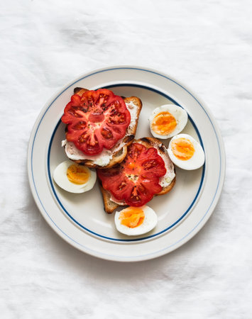 Delicious breakfast, snack - boiled eggs and sandwich with tomato on a light background, top view