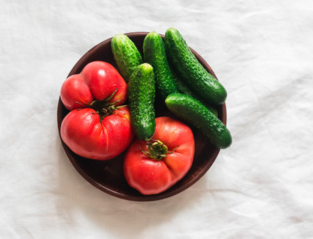 Fresh farm tomatoes and cucumbers in a clay bowl on a light background, top viewの写真素材
