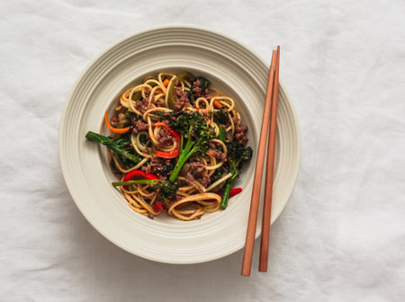 Egg noodles with ground beef, broccoli, sweet pepper, mushrooms in a bowl on a light background, top view. Asian style foodの写真素材