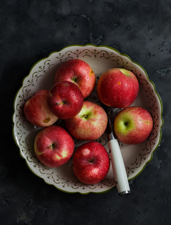 Fresh garden red apples in a bowl for baking on a dark table, top view