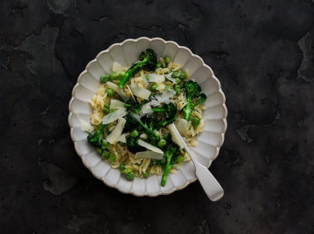 Delicious vegetarian lunch, dinner - orzo pasta with broccoli and green fresh peas on a dark background, top viewの写真素材