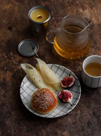 Cozy breakfast, snack - bun, figs, green tea and a candle on a wooden tableの写真素材