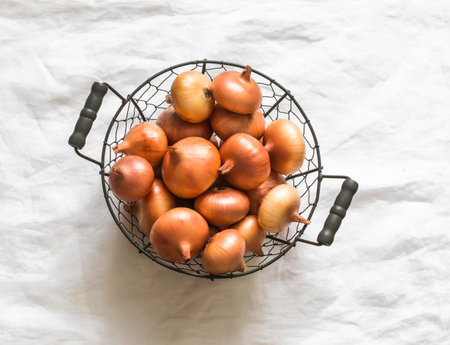 Onions in a metal basket on a light background, top viewの写真素材