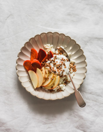 Delicious breakfast - cottage cheese with yogurt, apple, persimmon and granola on a light...