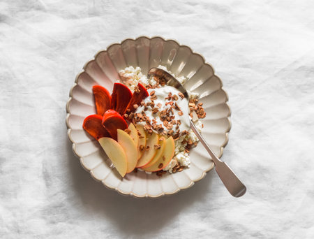 Delicious breakfast - cottage cheese with yogurt, apple, persimmon and granola on a light background, top viewの写真素材