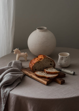 Sourdough bread, a candle, a vase, a cup on a round table with a gray tableclothの写真素材