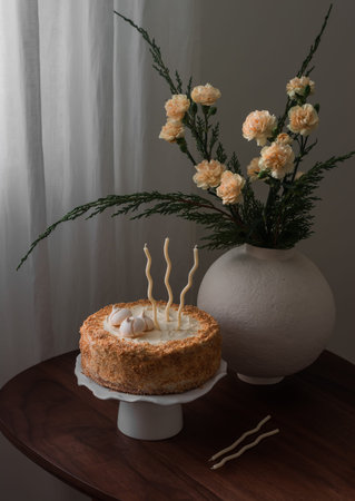 Birthday sponge cake with cream and bouquet of flowers on the wooden table in the living roomの写真素材