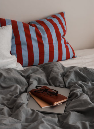 An unmade bed with bright lines, a laptop, a notebook. Cozy lazy morning concept