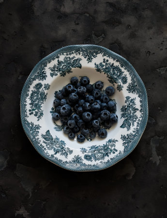 Fresh blueberries on a vintage plate on a dark background, top view