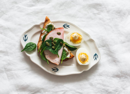 Delicious grilled breakfast - bread toast with cream cheese, spinach, ham, pumpkin seeds, boiled egg...