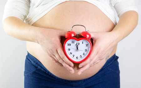 Pregnant woman\'s belly with alarm clock in shape of a heart