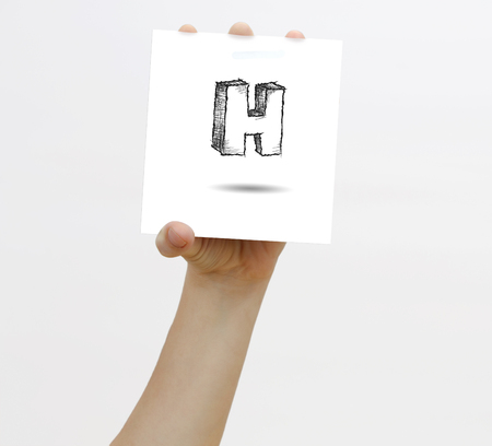 Hand holding a piece of paper with sketchy capital letter H, isolated on white.の写真素材