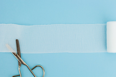 Medical scissors with unrolled gauze, on light blue background.の写真素材