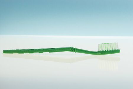 Green toothbrush on reflecting surface and light blue backgroundの写真素材