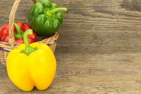 Fresh bell peppers in wicker basket, on wooden surface.の写真素材