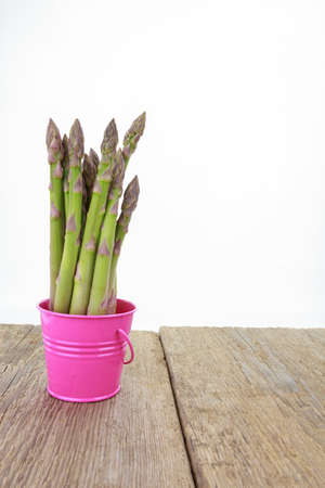 Asparagus spears in pink bucket on wooden surface, on white background with copy-spaceの写真素材