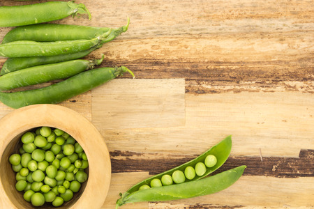 Fresh green peas in wooden bowl and pea pods, on wooden surfaceの写真素材