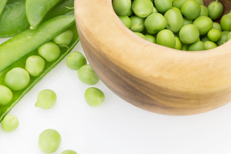 Fresh green pea pods and peas in wooden bowl closeup, on white backgroundの写真素材