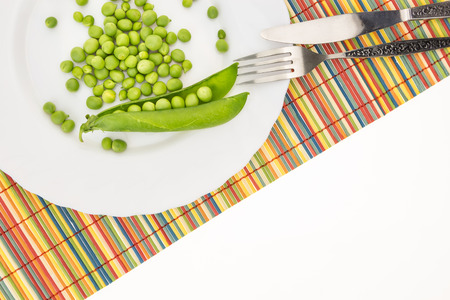 Fresh green peas on plate with fork and knife closeup, on colorful bamboo placemat with copy-spaceの写真素材