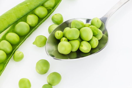 Fresh green peas in spoon closeup and a pea pod, on white backgroundの写真素材