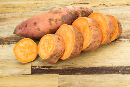 Fresh sweet potatoes whole and sliced , on wooden backgroundの写真素材
